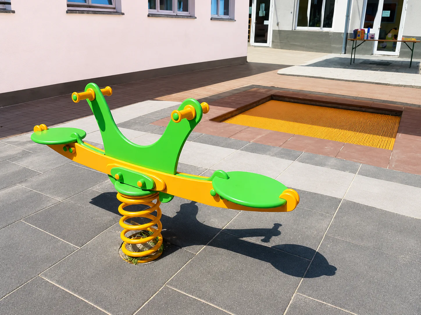 Grün-gelbe Wippe und Bodentrampolin im CityKids-Außengelände